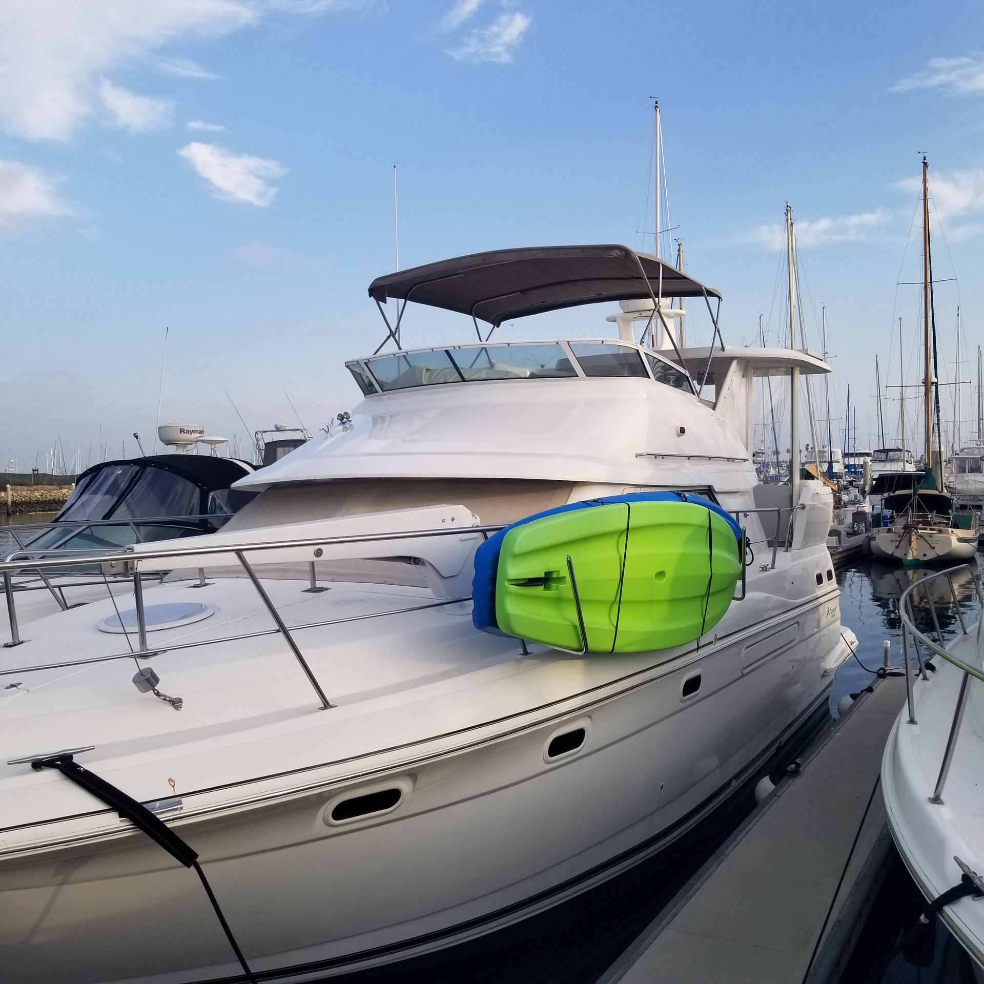 White motor yacht with a brown canopy docked at a marina; a green kayak is mounted on the side.