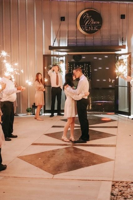 Couple slow dancing in a warmly lit event hall, with guests and sparklers in the background
