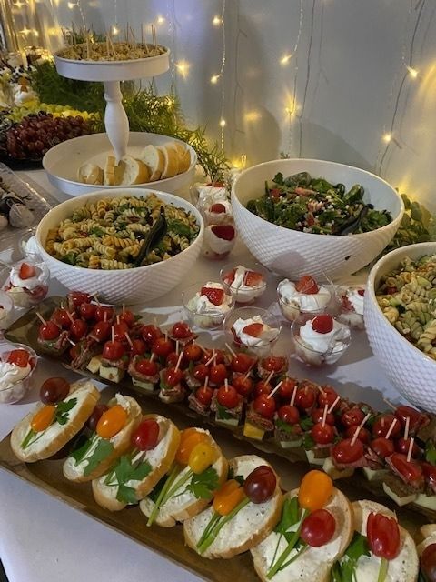 Buffet table with caprese skewers, stuffed mini cups, salads, and desserts under warm string lights