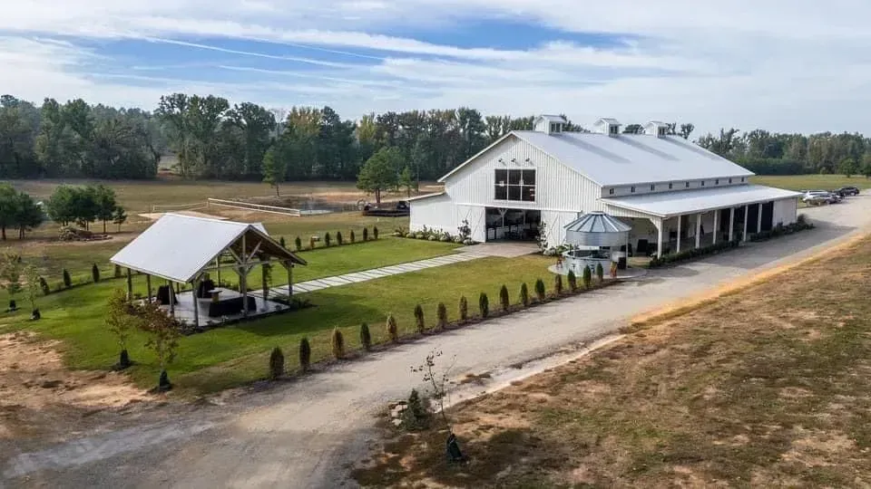 Large white barn-style building with tented patio and fenced lawn in a rural landscape