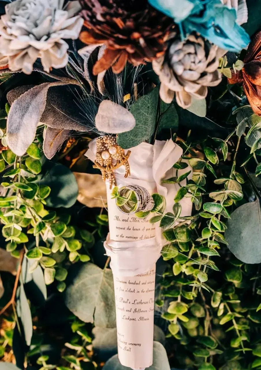 A bridal bouquet with white and teal flowers, greenery, and a hanging personalized tag.