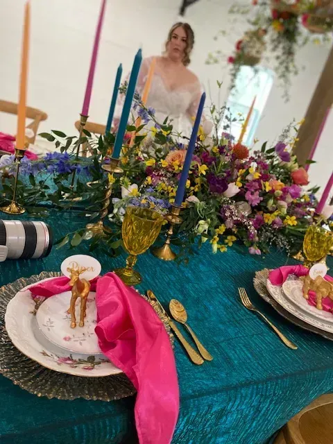 Elegant table setting with teal tablecloth, gold accents, pink napkins, candles, and floral centerpiece