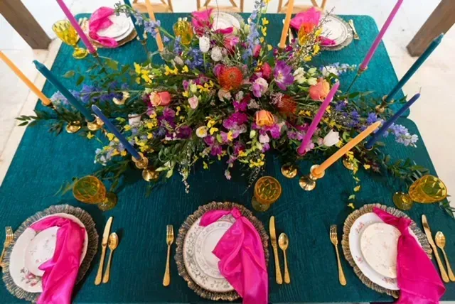 Colorful floral table centerpiece with tall candles and gold accents on a teal table setting