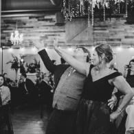 Couple dancing at a wedding reception, smiling and raising their arms in a decorated hall
