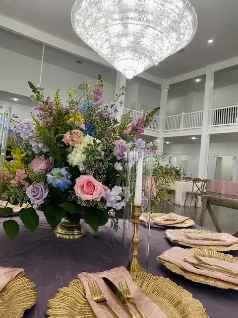 Lavish banquet table with purple decor, gold place settings, and a large floral arrangement under a chandelier