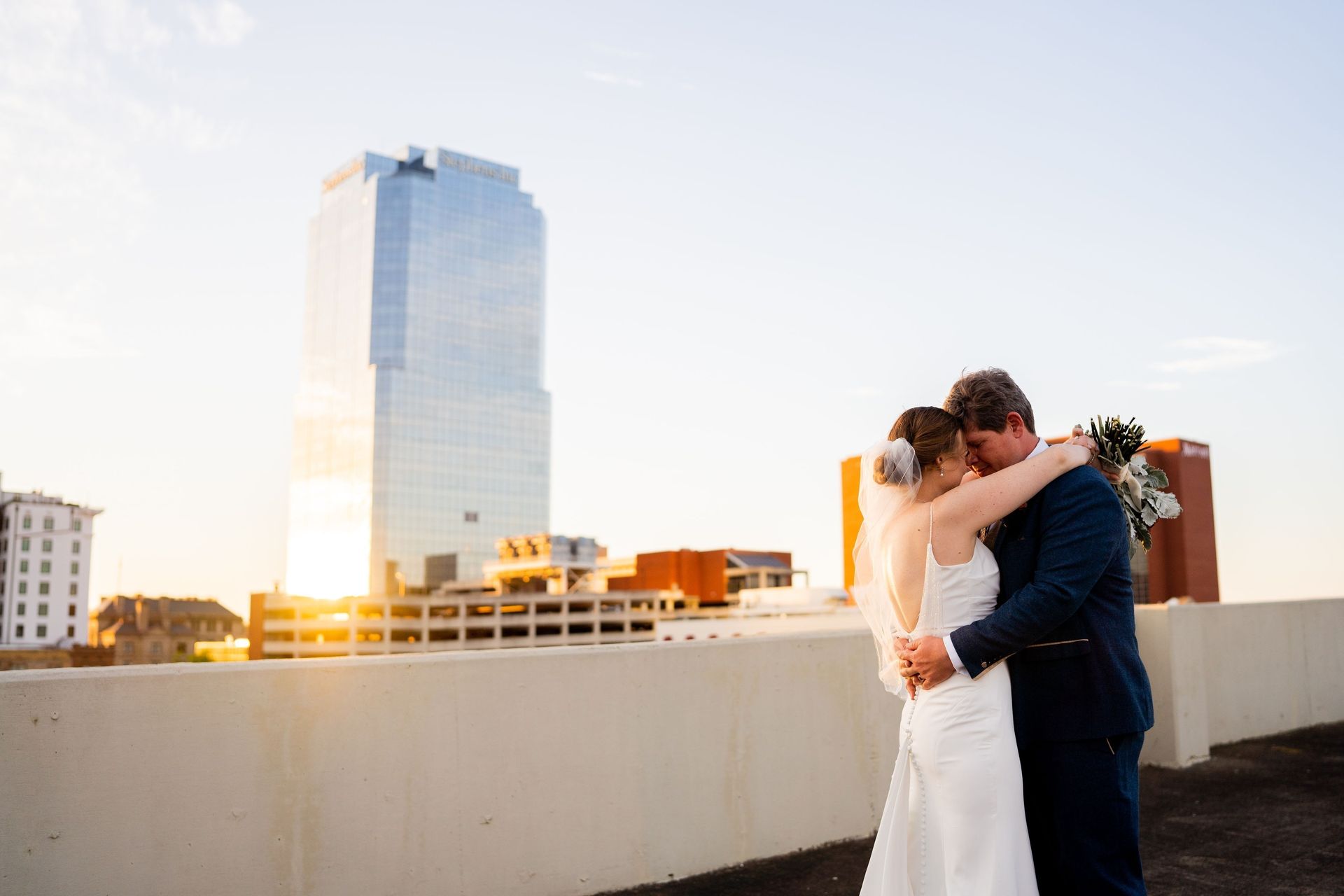 Couple embracing on a rooftop at sunset with a city skyline behind them