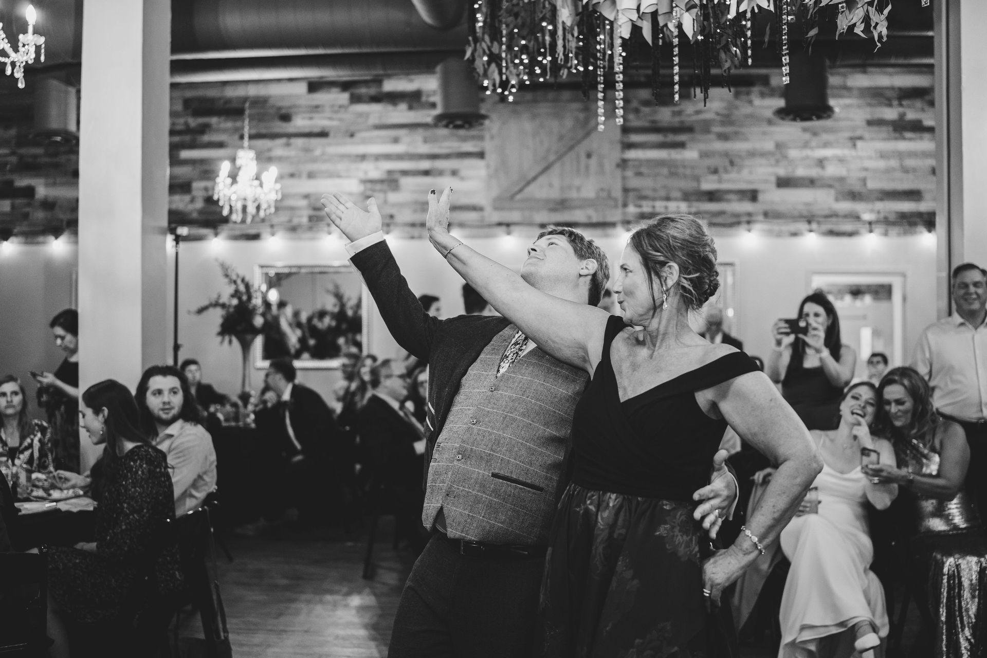 People dancing at a lively indoor event, with guests seated at tables in the background.