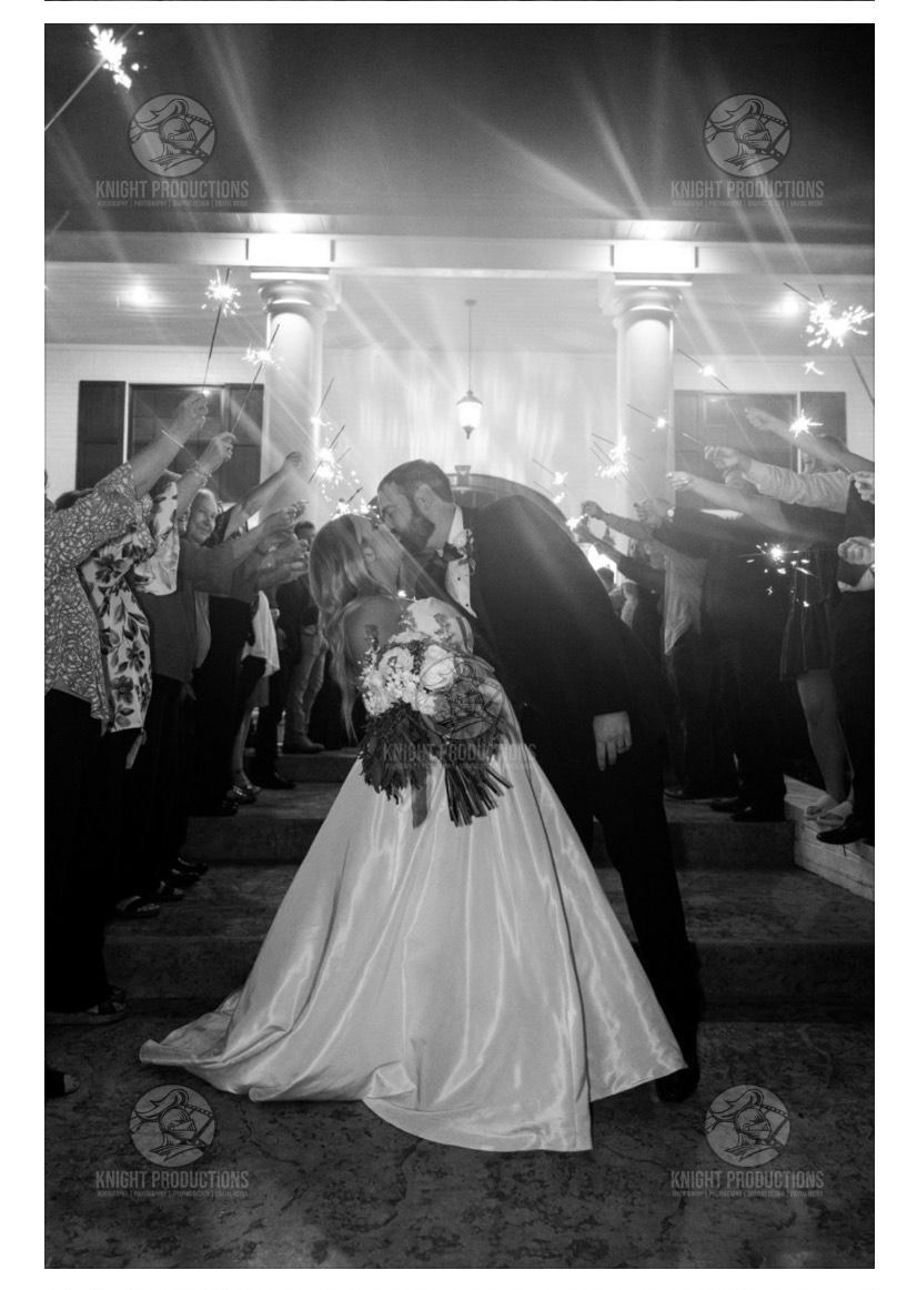 Bride and groom kiss at the altar, surrounded by guests under bright lights.