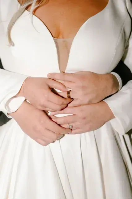Close-up of two hands with rings holding a white dress with a deep V neckline