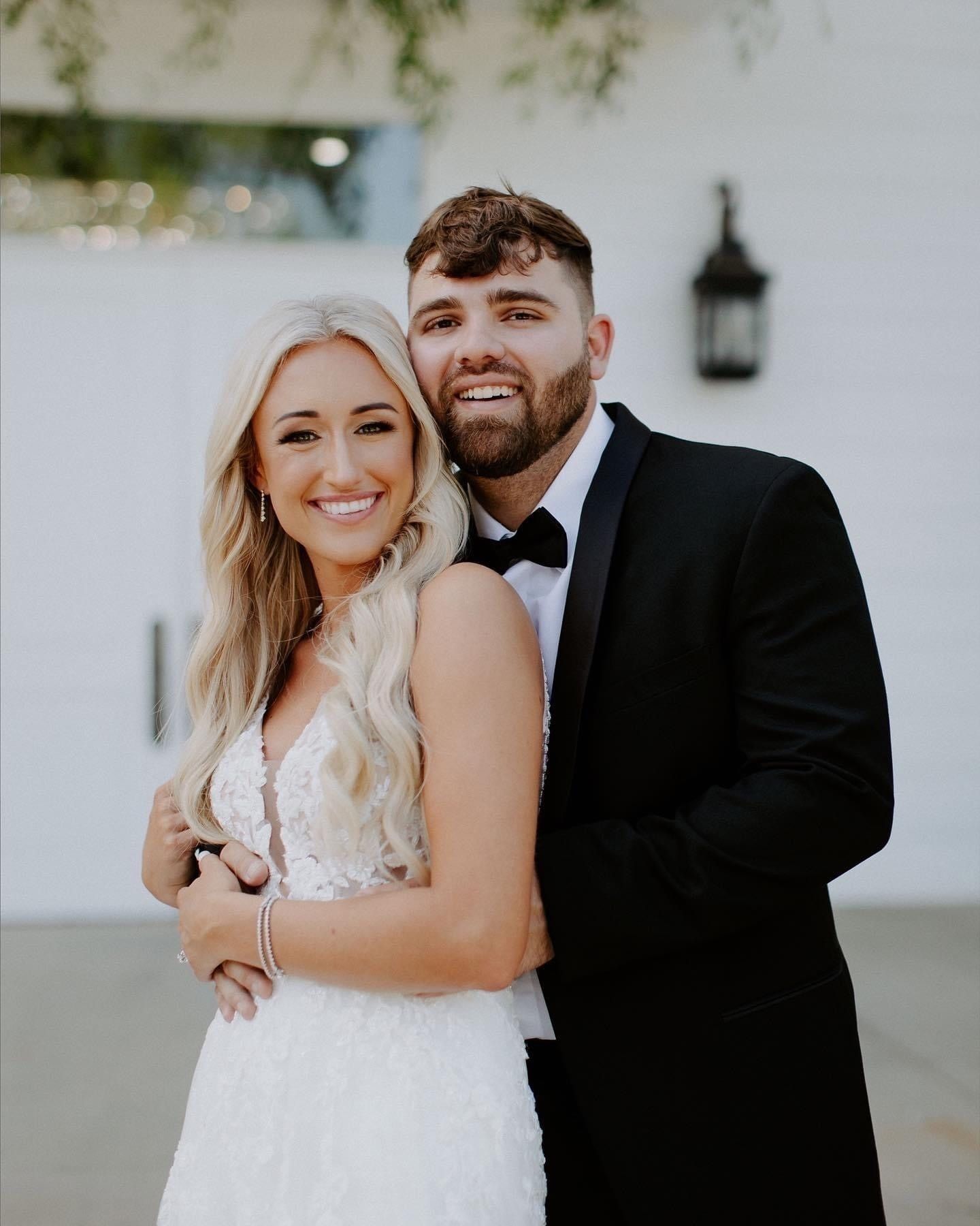 Smiling couple in wedding attire embracing outdoors by a white building