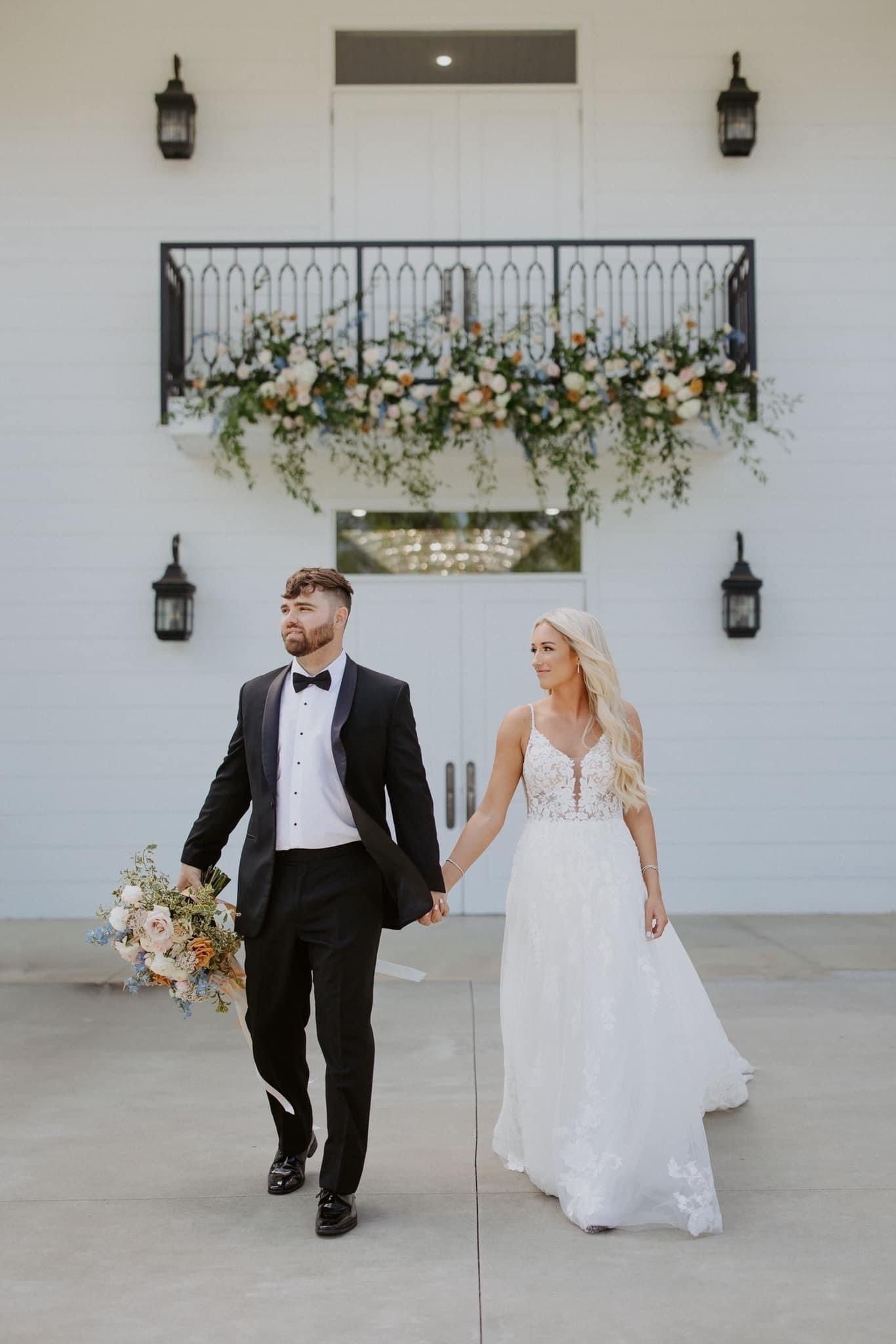 Bride and groom walking hand in hand outside a white building with floral balcony decor