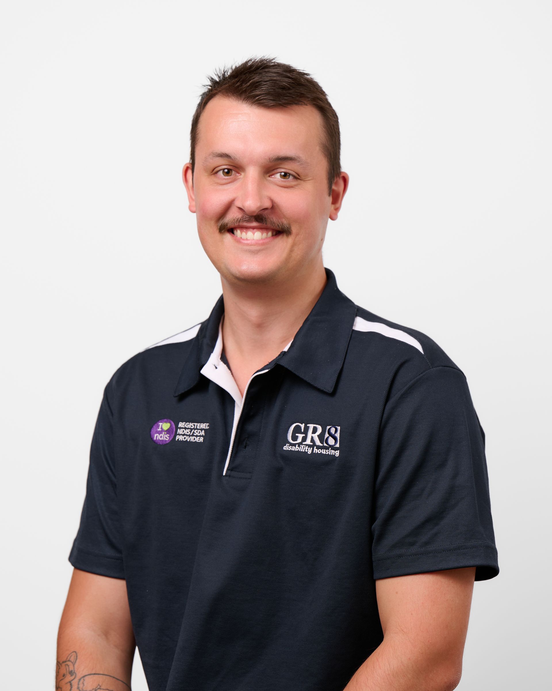 A man with a mustache is wearing a white shirt and smiling.