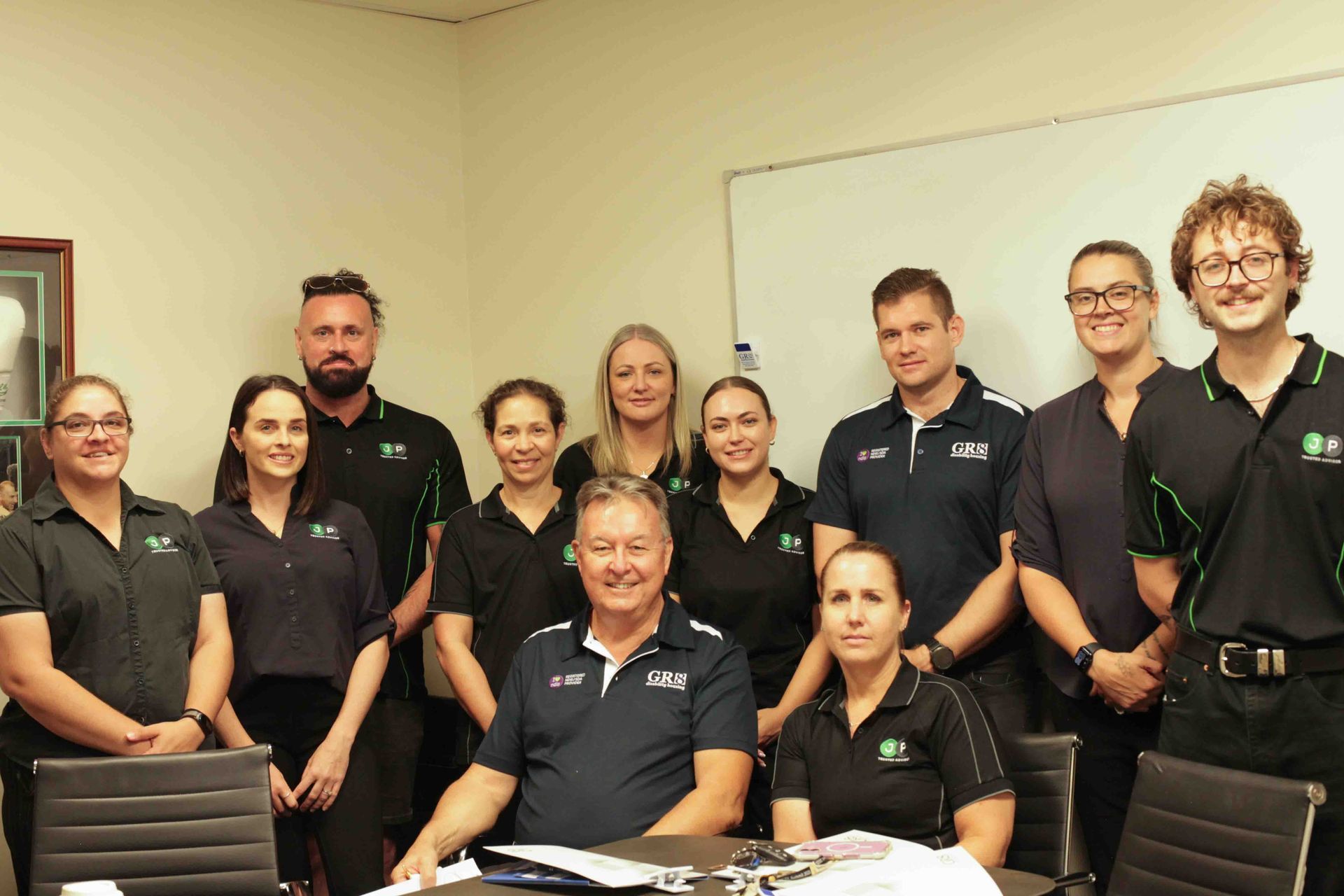 A group of professionals in polo shirts standing and sitting together in an office setting.