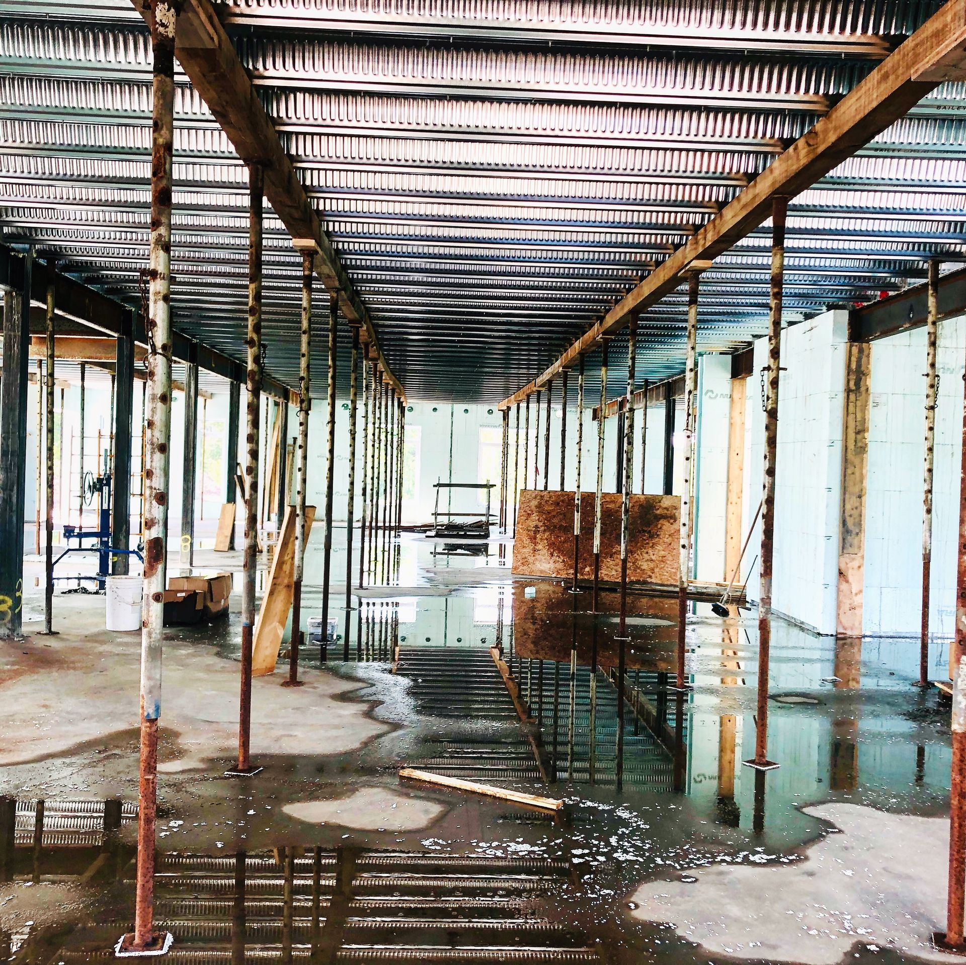 Intérieur d'un chantier de construction avec des supports temporaires, un plafond ondulé et un sol mouillé reflétant la scène.