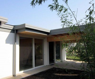 Moderno edificio bianco con ampie finestre, tettoia in legno e piante di bambù.