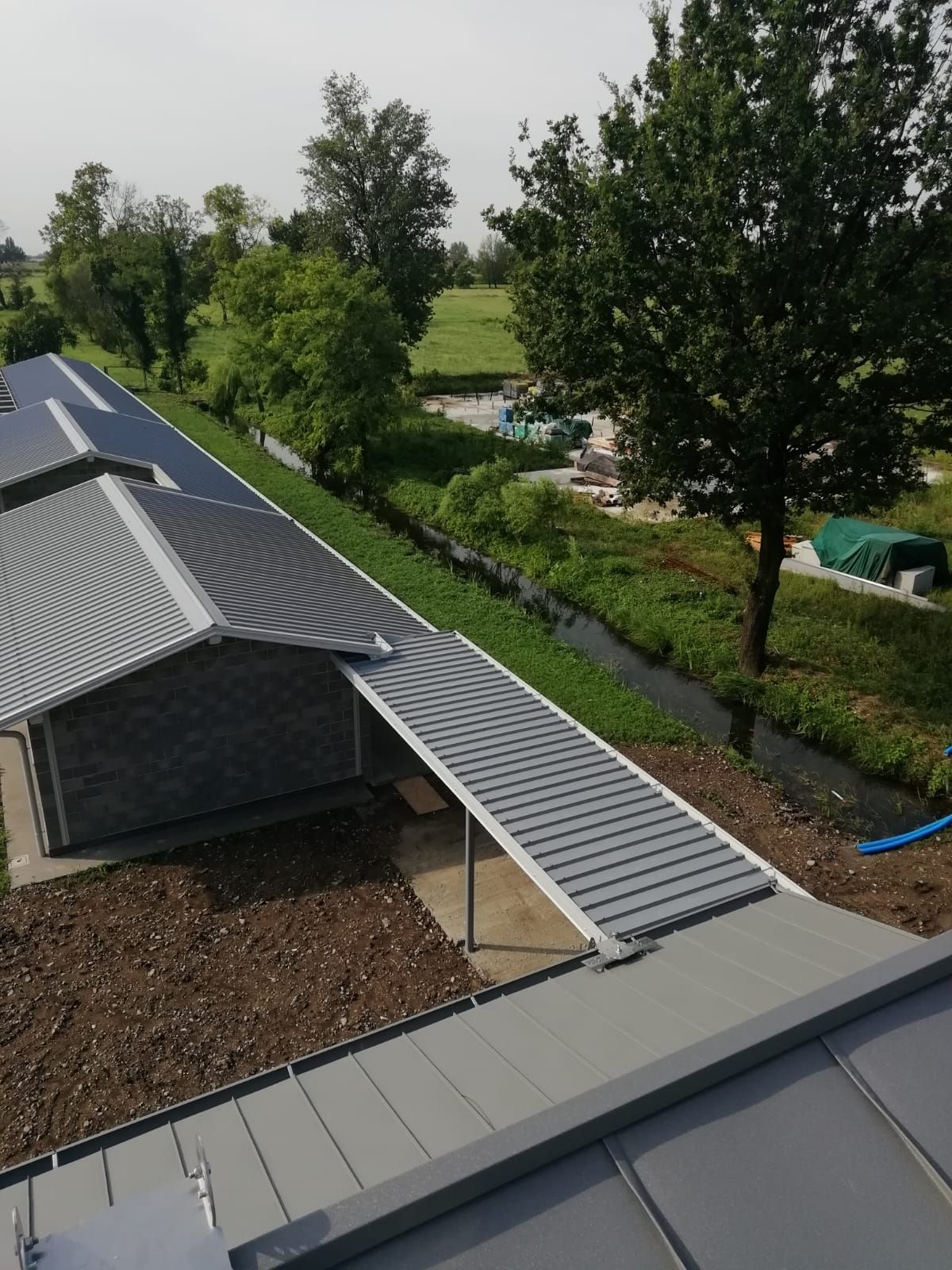 Vista dall'alto di un edificio con pannelli solari sul tetto. Una lunga struttura grigia si estende verso l'esterno. Sullo sfondo si vedono alberi e un corso d'acqua.