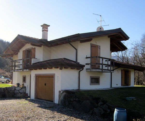 Casa a due piani con finiture in legno e balcone. Portone del garage marrone, camino e antenna sul tetto. Giornata di sole.