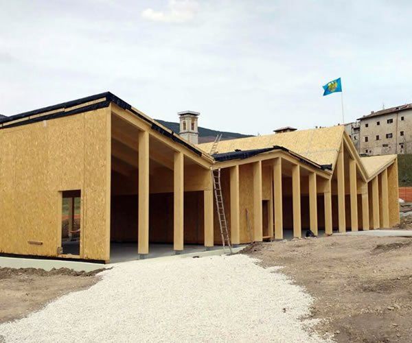 Edificio con struttura in legno in costruzione, tetti spioventi, lato aperto e bandiera.