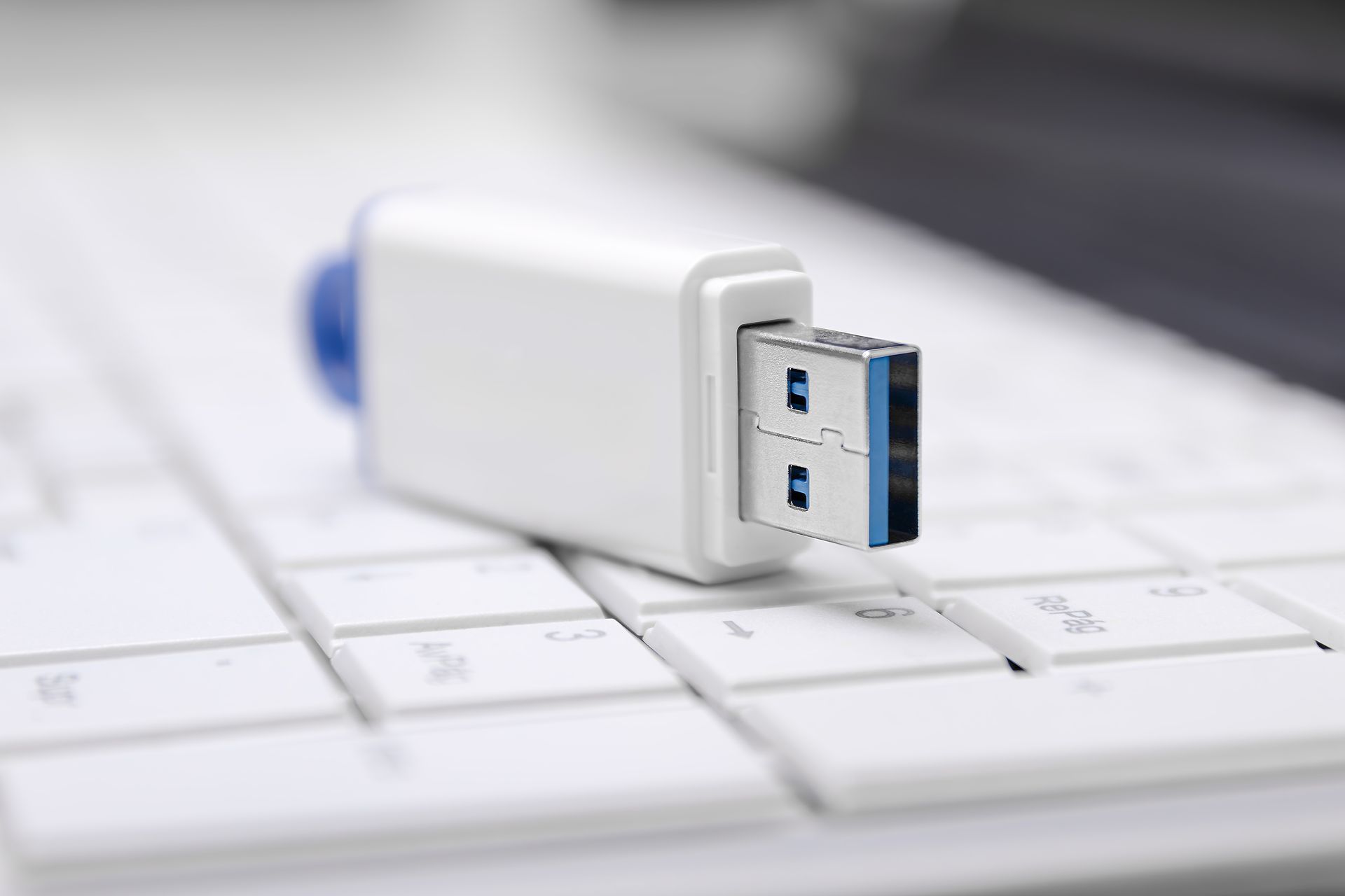 White USB flash drive on a white computer keyboard.