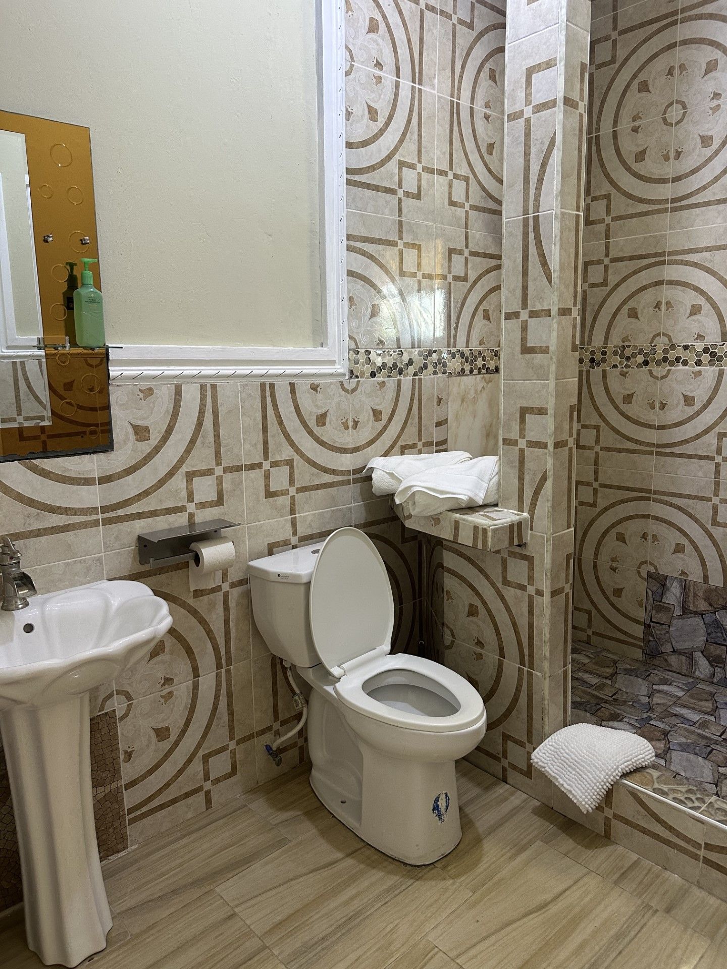 A bathroom with a toilet , sink , mirror and shower.