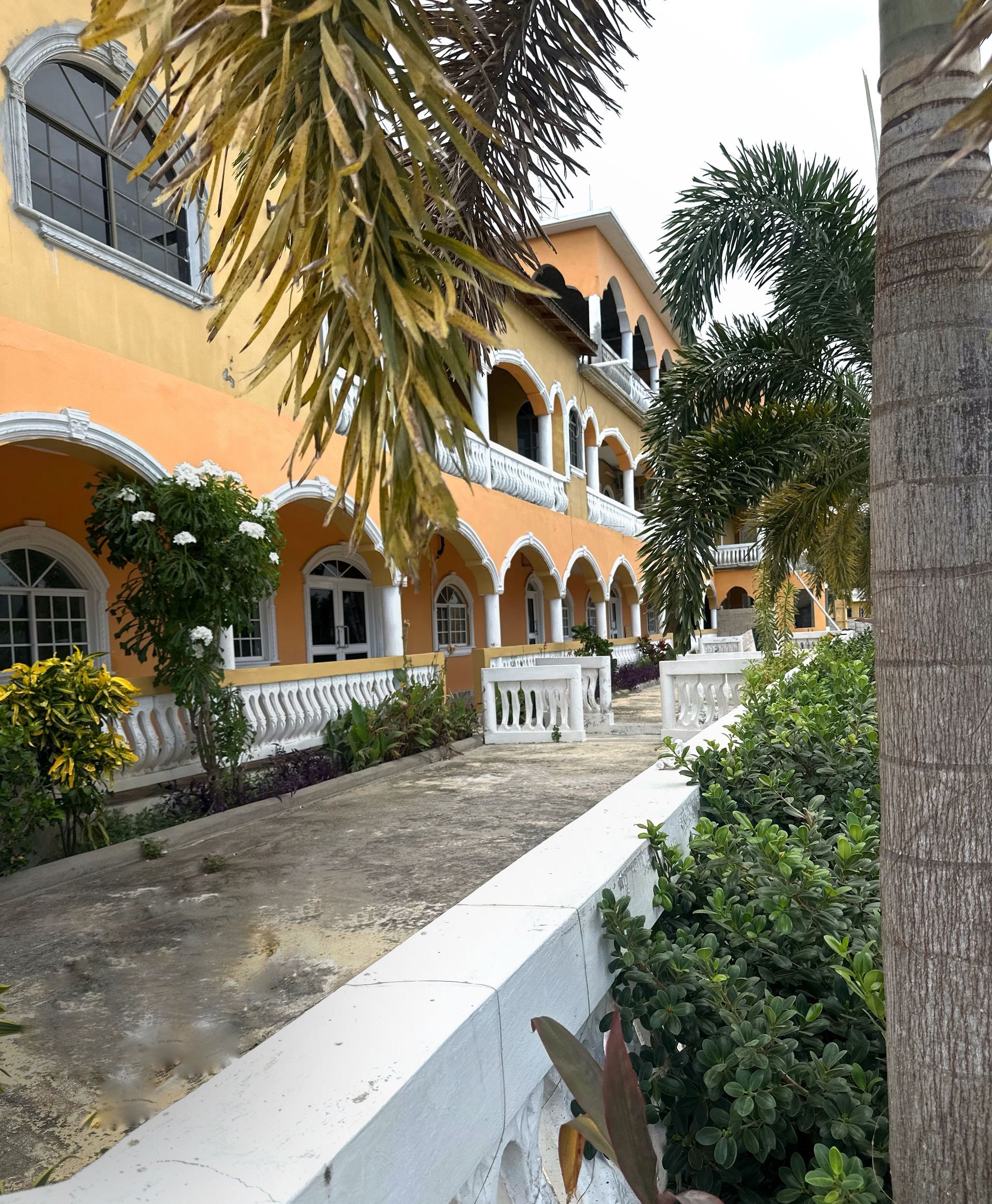 A large orange building with arched windows is surrounded by trees and bushes.