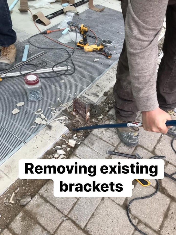A person is removing existing brackets from a brick walkway.