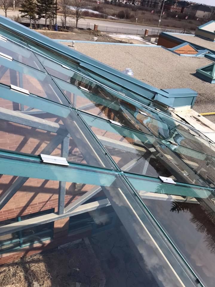 Glass roof with blue trim and exposed beams, reflecting the sky and building interior.