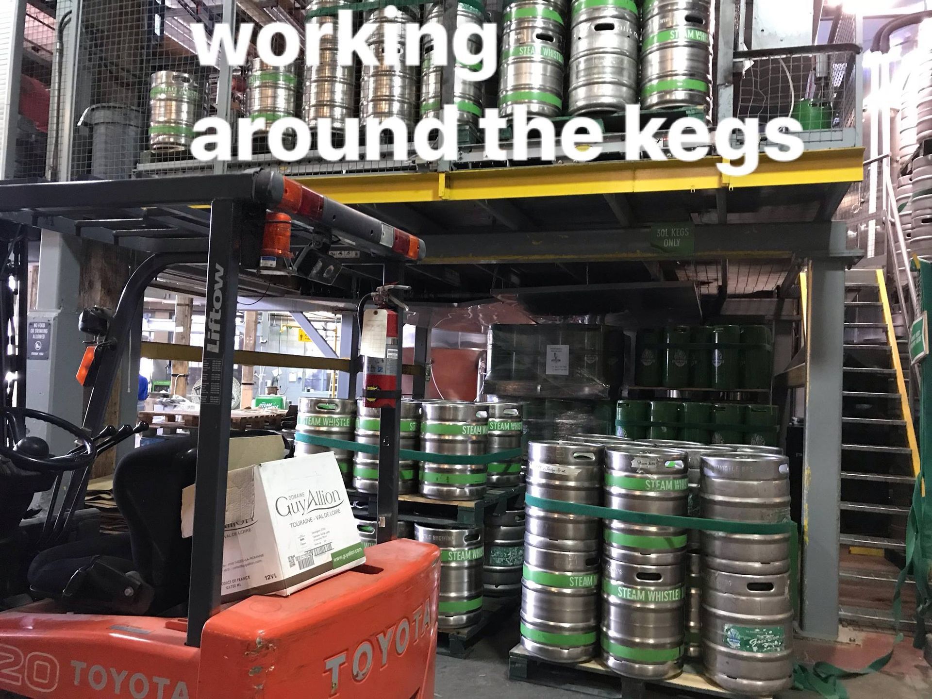 A forklift is working around the kegs in a warehouse.