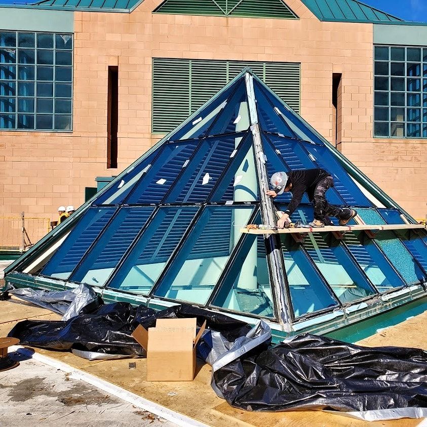 A man is working on a glass pyramid in front of a building