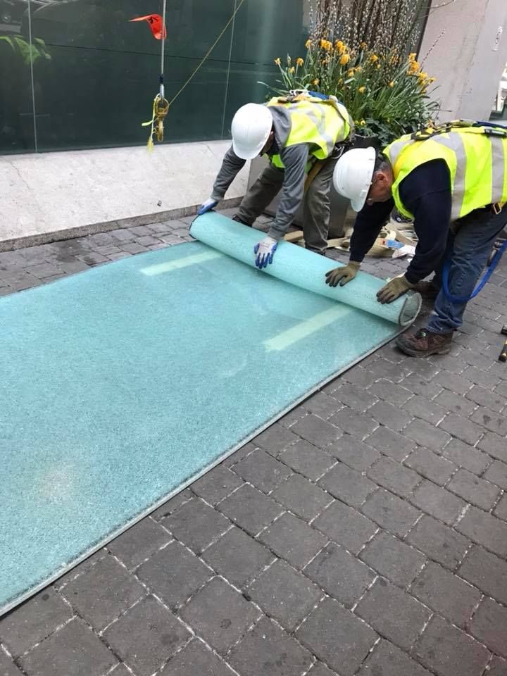 Two construction workers are working on a carpet on a sidewalk