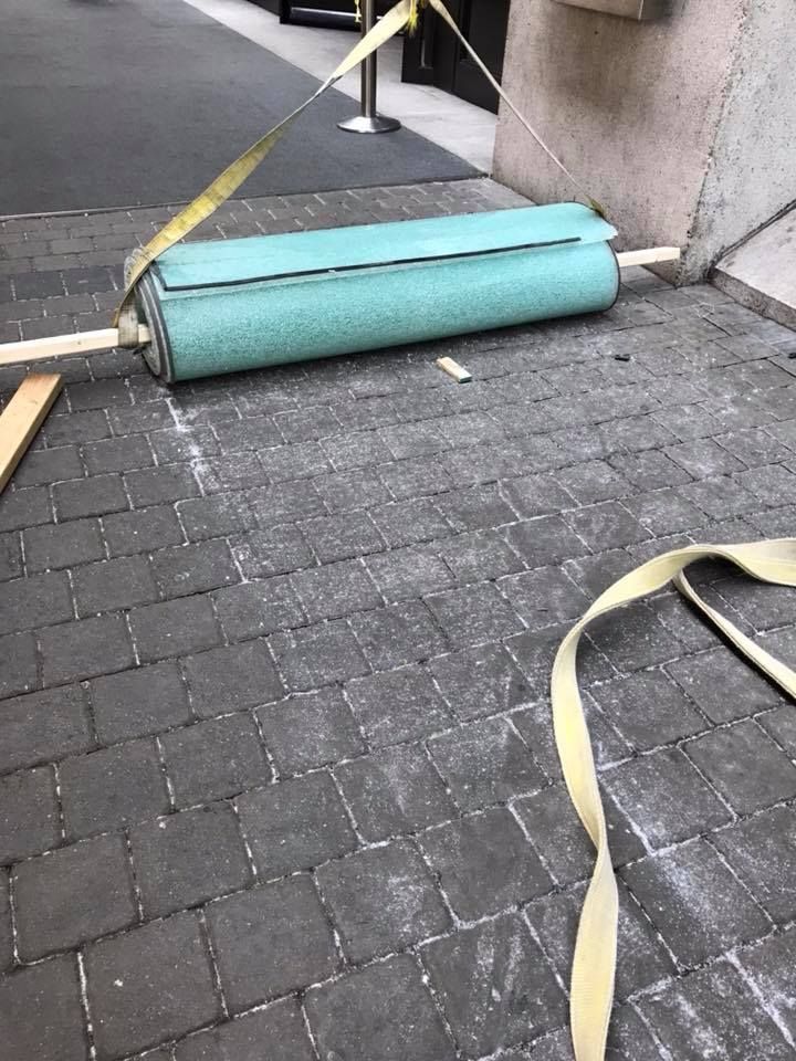 A roll of green carpet is laying on a brick sidewalk.