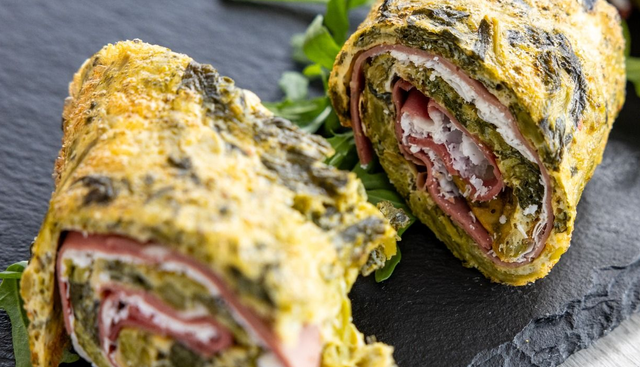 Piadina a fette ricoperta di erbe aromatiche, farcita con carne e formaggio e servita su un tagliere di ardesia scura.