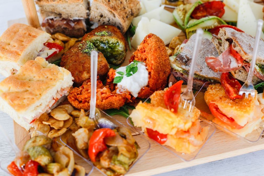 Un assortimento di stuzzichini monoporzione serviti su un piatto, tra cui panini, fritti e contorni di verdure.