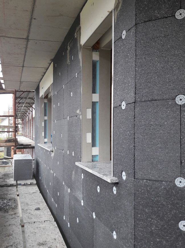Esterno di un edificio con facciata in pietra, grondaie marroni e tubi arancioni in una giornata di sole.