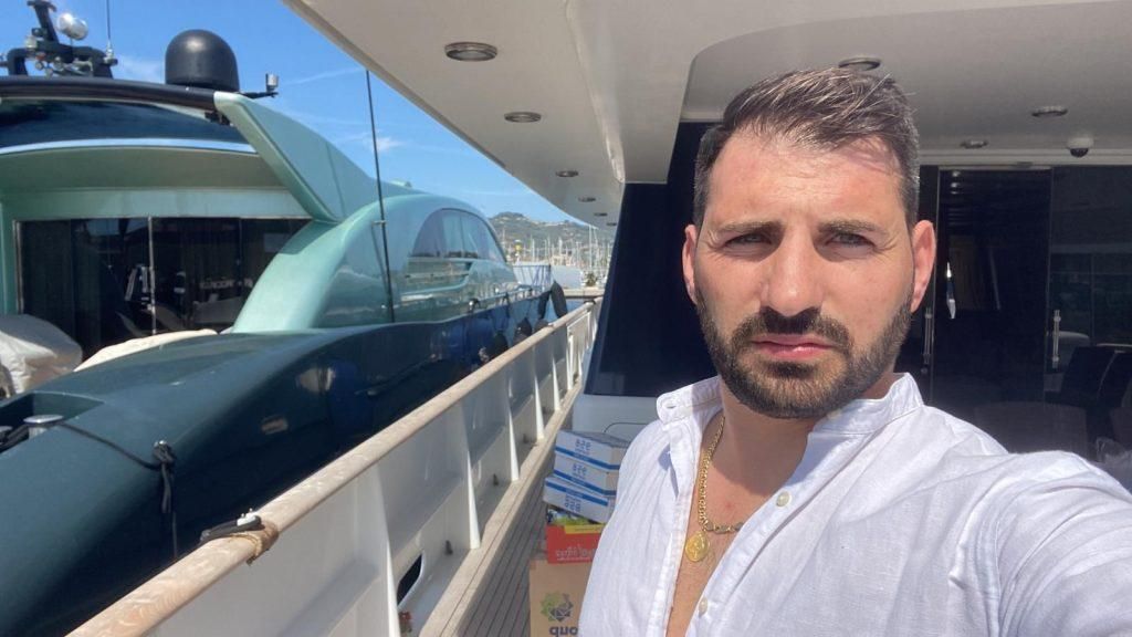 Uomo su uno yacht, con indosso una camicia bianca.