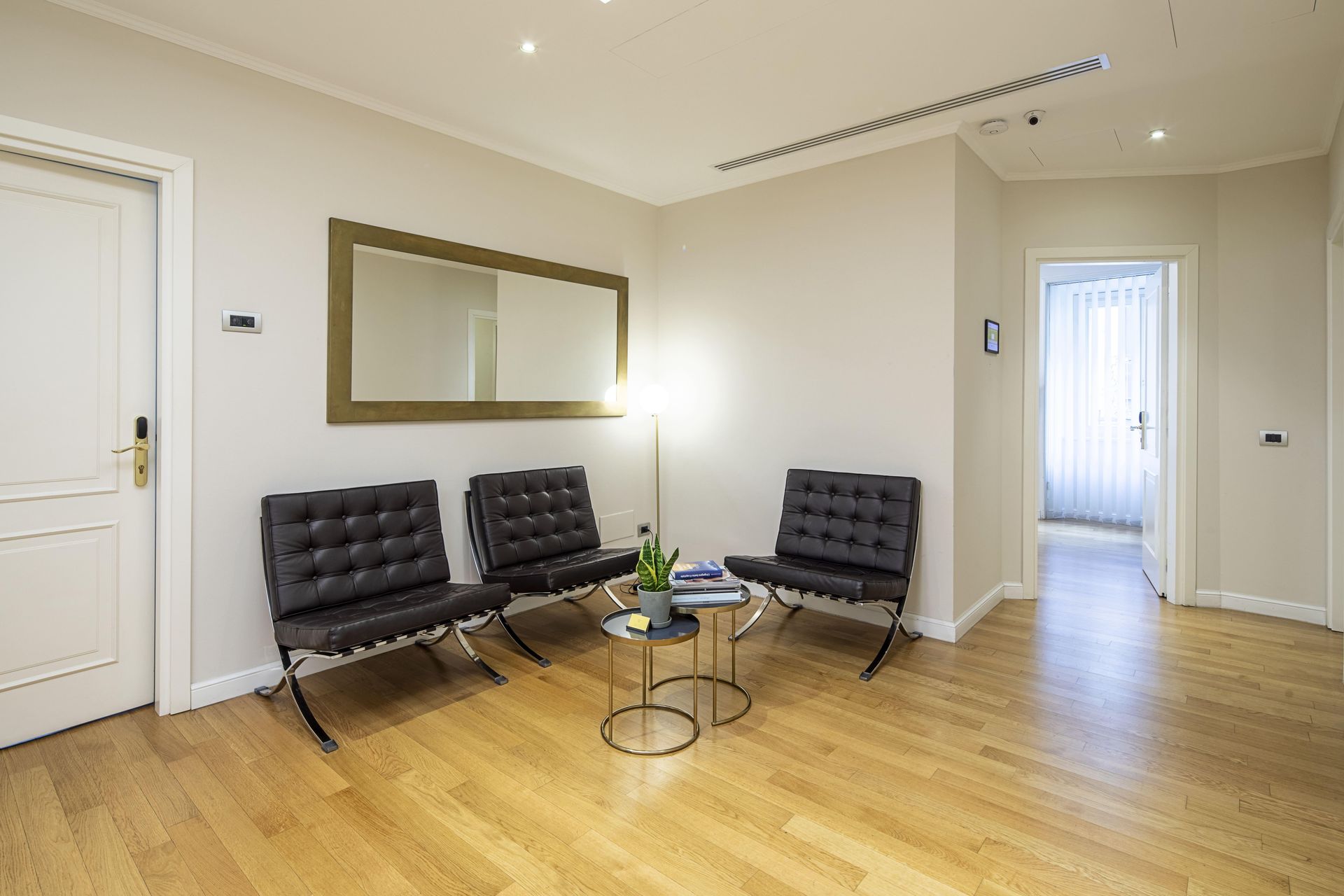 Sala d'attesa con sedie in pelle nera, uno specchio e un tavolino.