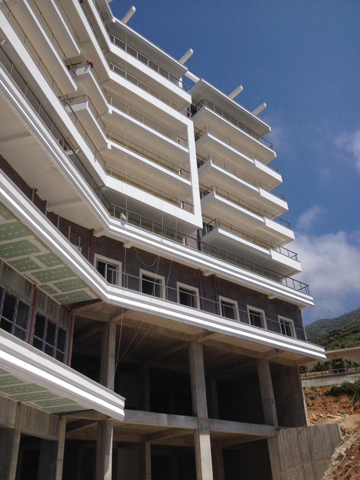 Edificio in costruzione; balconi bianchi su una struttura a più piani con pareti esterne marroni contro un cielo azzurro.