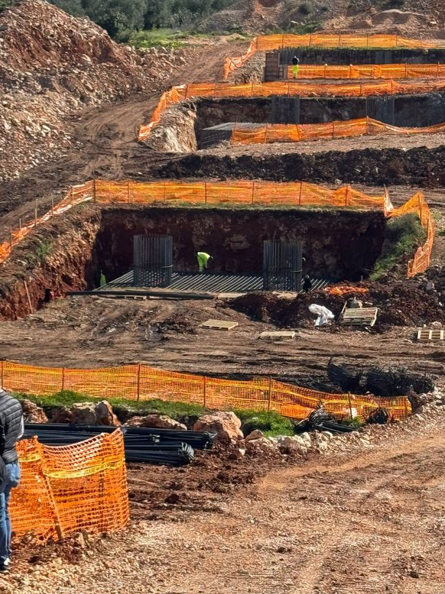 Esterno di un edificio con facciata in pietra, grondaie marroni e tubi arancioni in una giornata di sole.