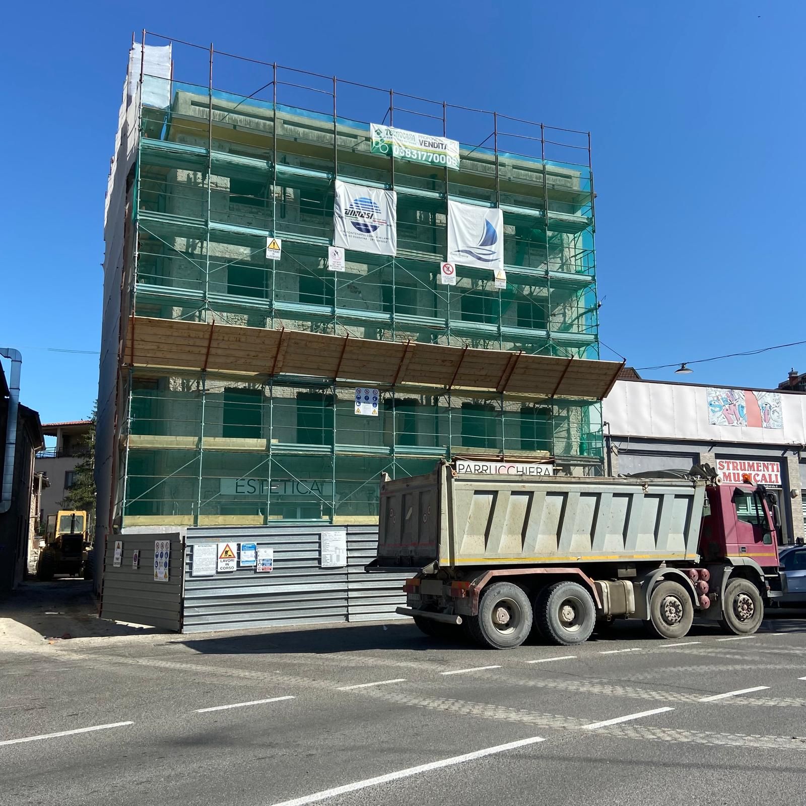 Edificio in costruzione; balconi bianchi su una struttura a più piani con pareti esterne marroni contro un cielo azzurro.