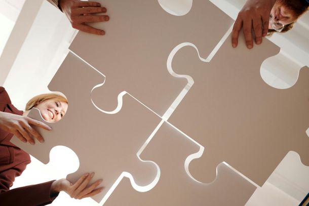 Persone che tengono in mano pezzi di puzzle, collaborano, sorridono.