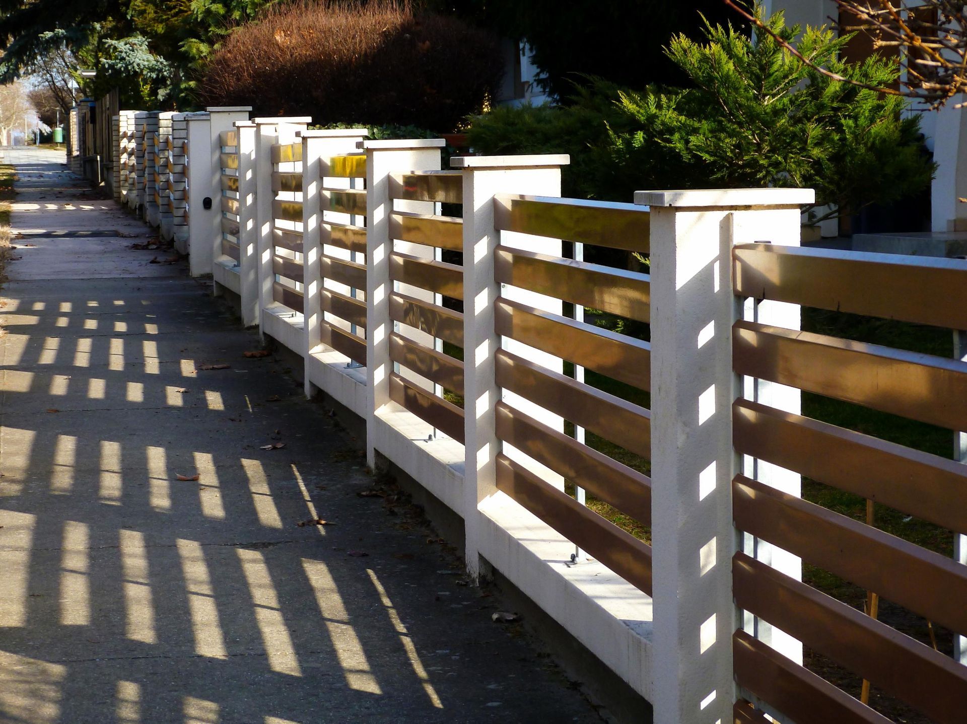 Wooden slat fence with concrete posts casting shadows on the sidewalk.
