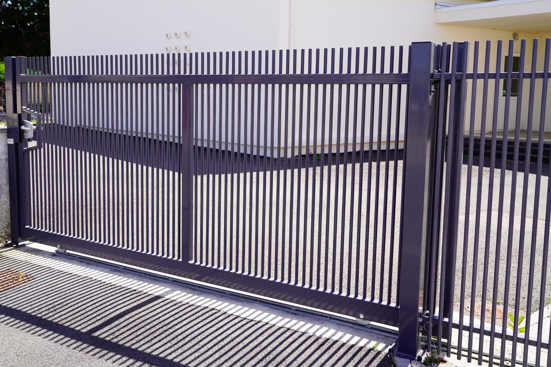 Dark gray metal gate with vertical bars, casting shadows on the ground.