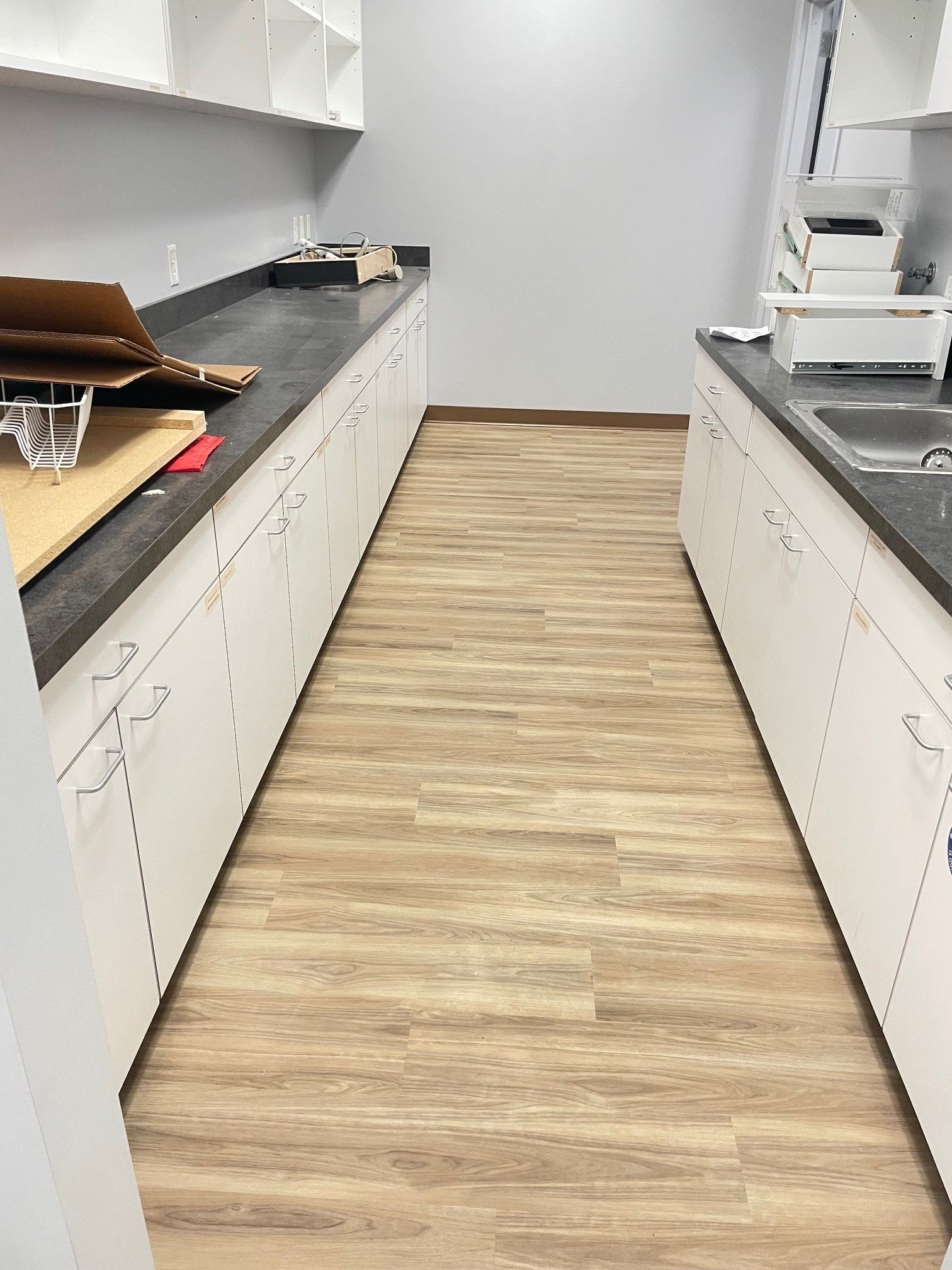 A long kitchen with wooden floors and white cabinets.