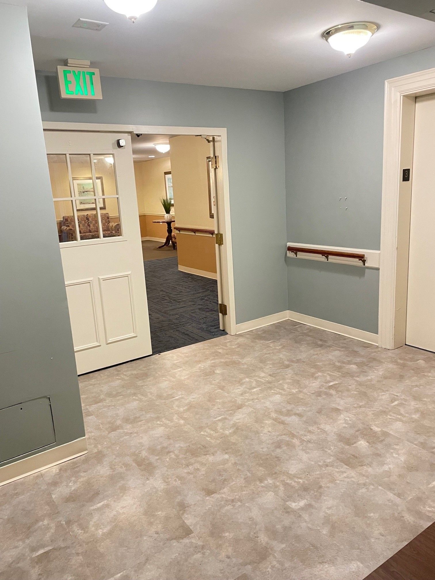 A hallway with a green exit sign above the door.