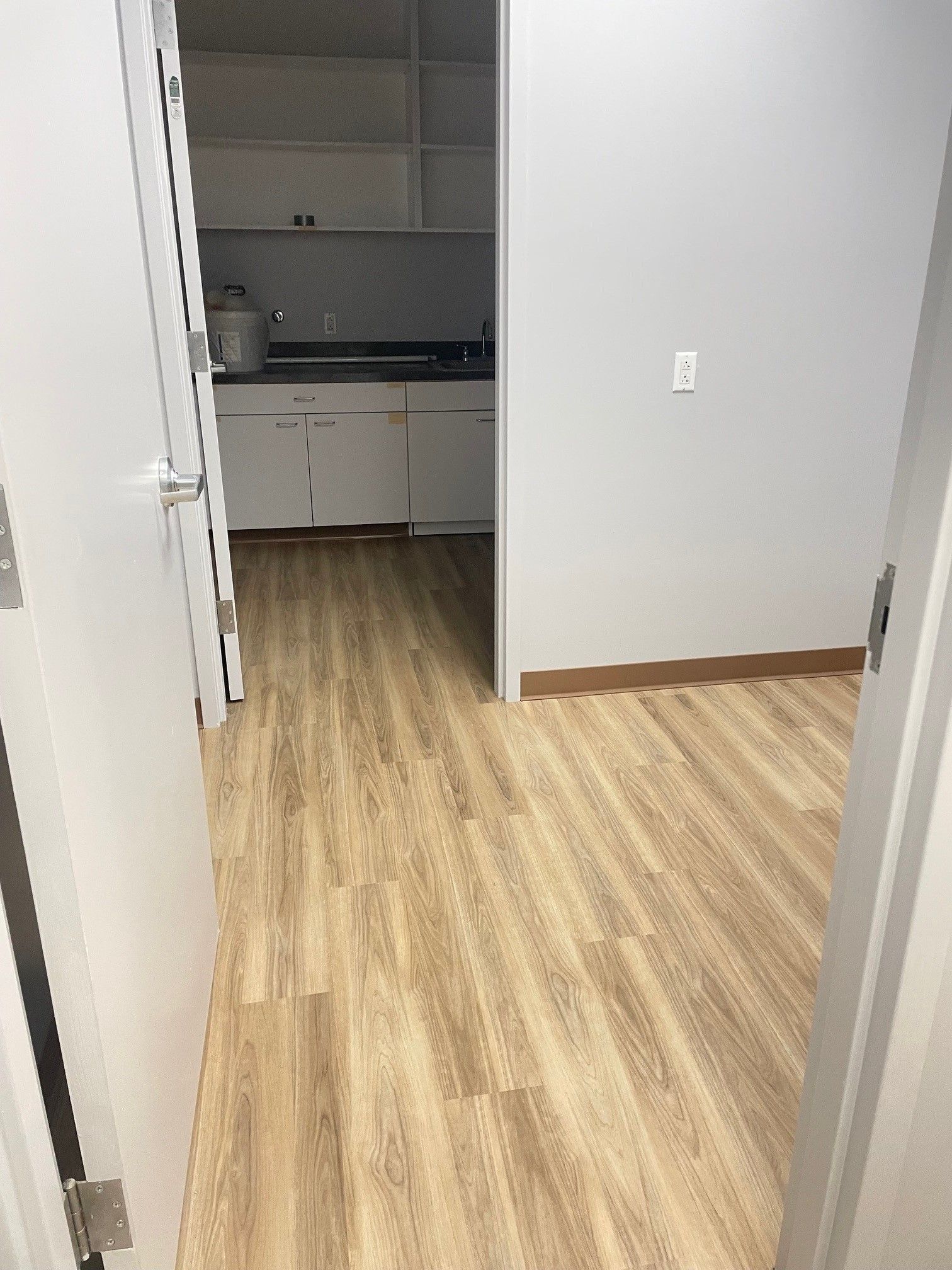 A hallway leading to a kitchen with hardwood floors and white cabinets.