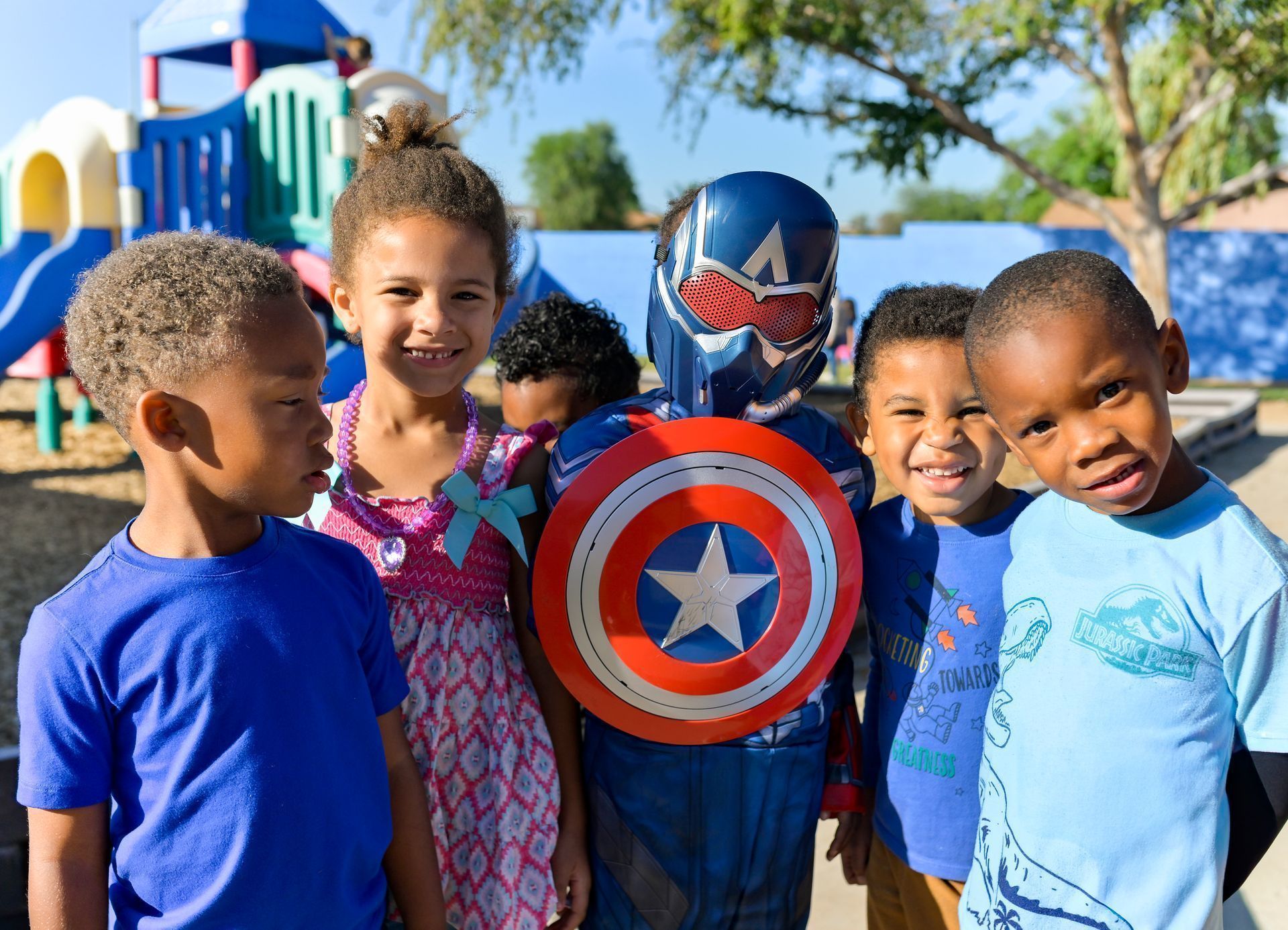 Children posing outdoors with Captain America shield and costume at a sunny event