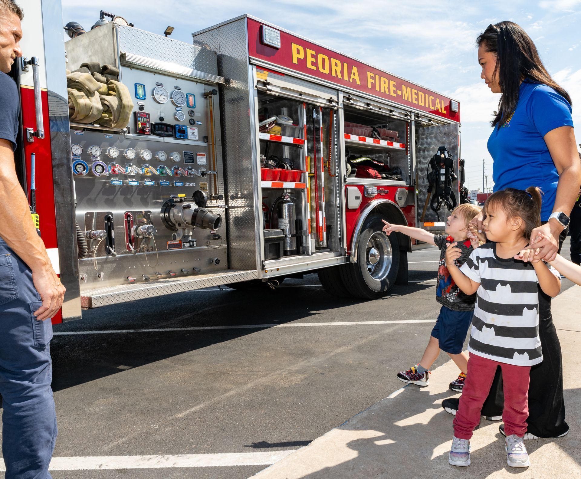Fire truck parked roadside with children and adults looking at its equipment display