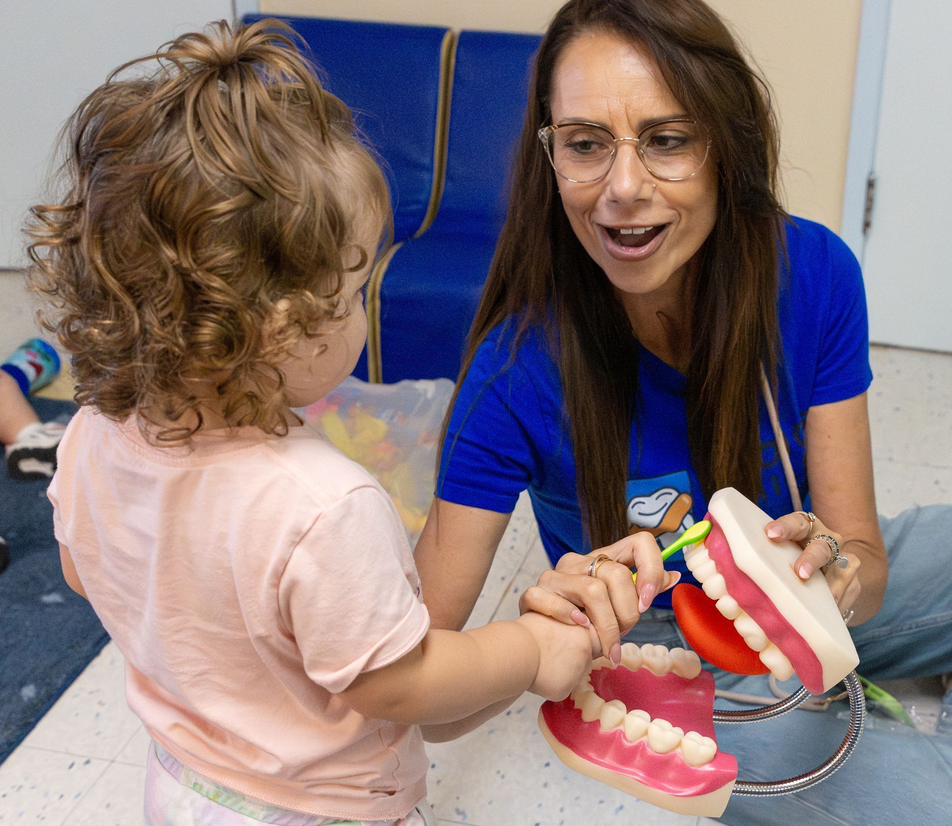 Woman and toddler with dental model, learning to brush teeth in a classroom setting