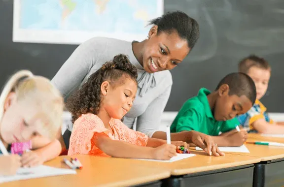Teacher helping students write at a classroom table