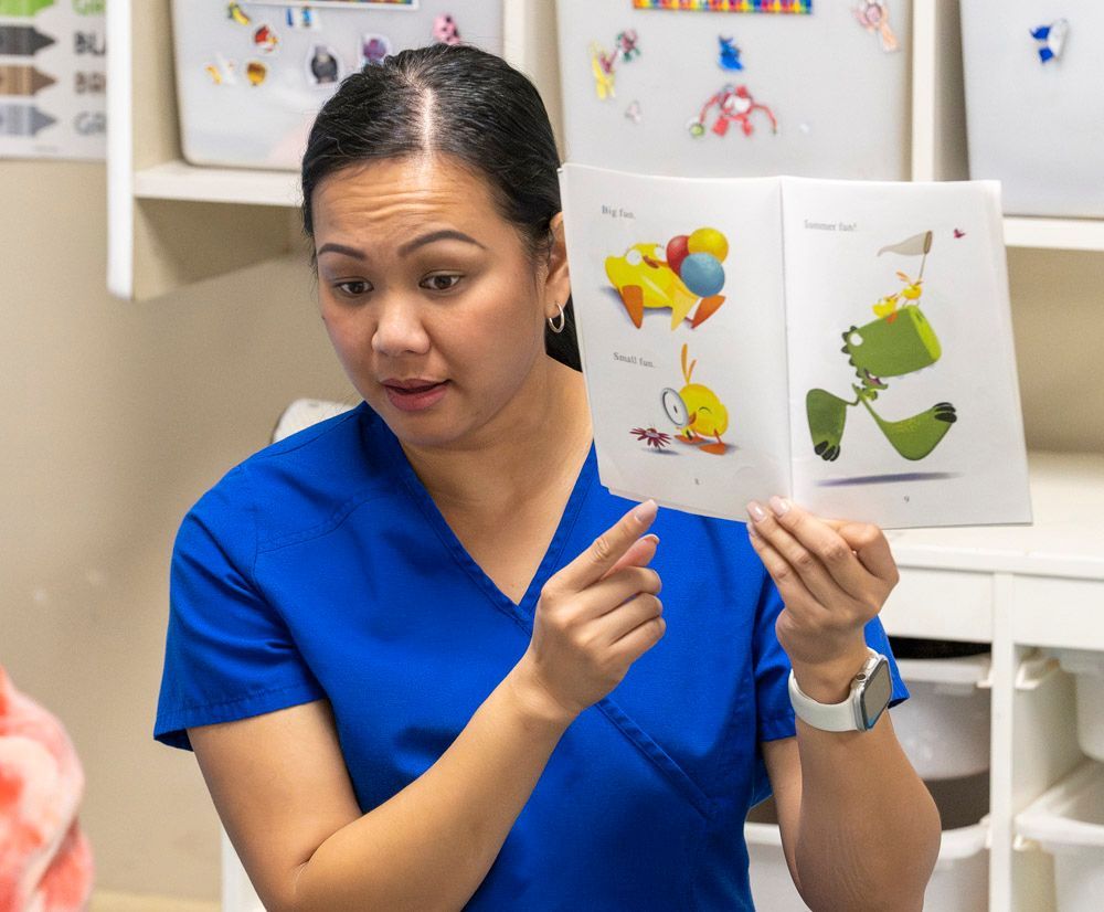 Woman in blue scrubs showing illustrated pages to a child in a clinic room
